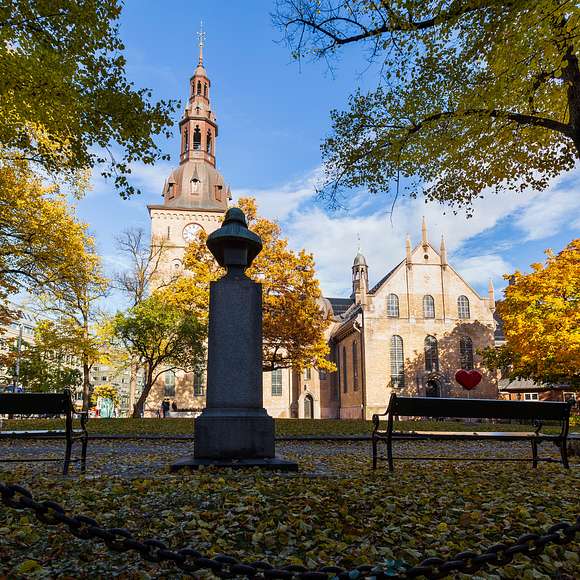 Brick church framed by golden trees and park benches under a clear blue sky.