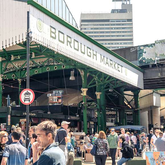A bustling crowd gathers outside Borough Market on a sunny day, surrounded by street signs and market stalls.