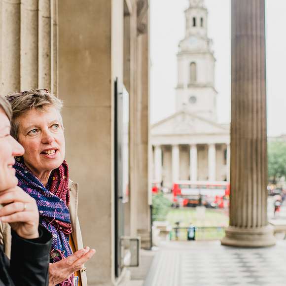 Two women talk with columns of the National Gallery behind them and St. Martin-in-the-Fields church in the distance.