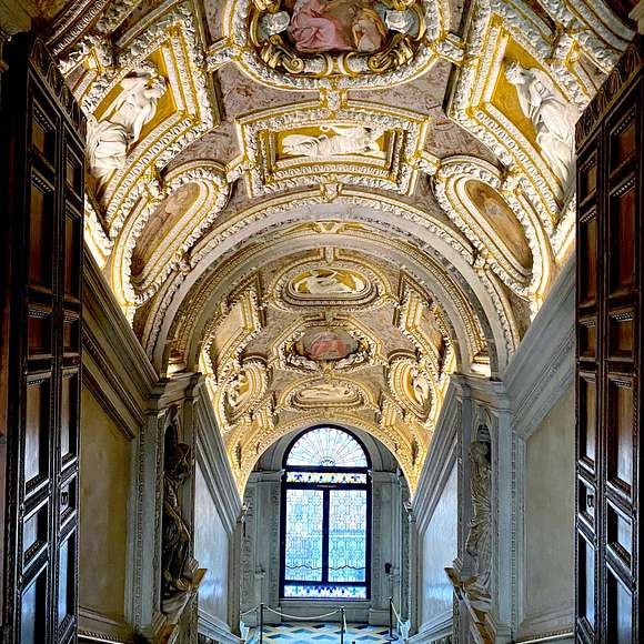 Ornate staircase inside the Doge's Palace in Venice, featuring a richly decorated vaulted ceiling with gold stucco, sculptures, and a stained-glass window at the bottom.