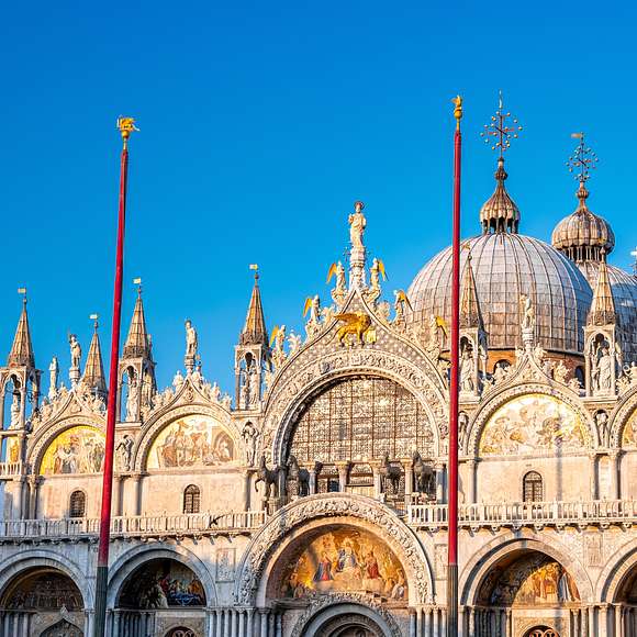 St. Mark’s Basilica glowing at golden hour, with domes, mosaics, and statues shining against a blue sky.