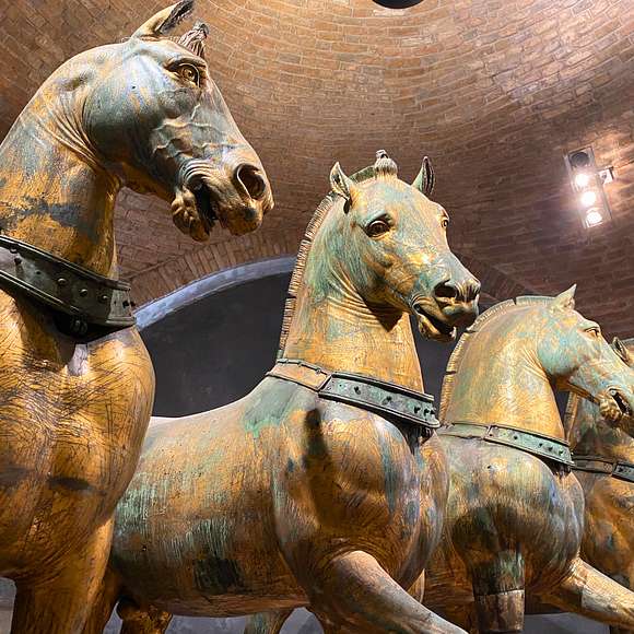 Ancient bronze Horses of Saint Mark inside the basilica, set against a vaulted brick ceiling and museum lighting.