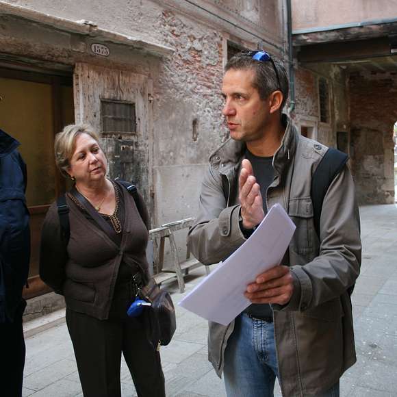 A guide explains Cannaregio’s history to two visitors in a quiet alleyway.