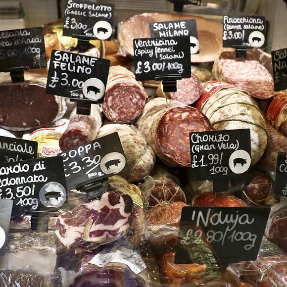 Display of artisanal cured meats with handwritten price tags at a deli counter during a London food tour stop.